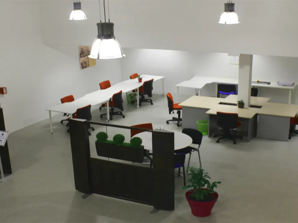 Plateau d'un espace de coworking à Toulouse : rangées de bureaux blancs partagés, chaises orange et suspensions industrielles